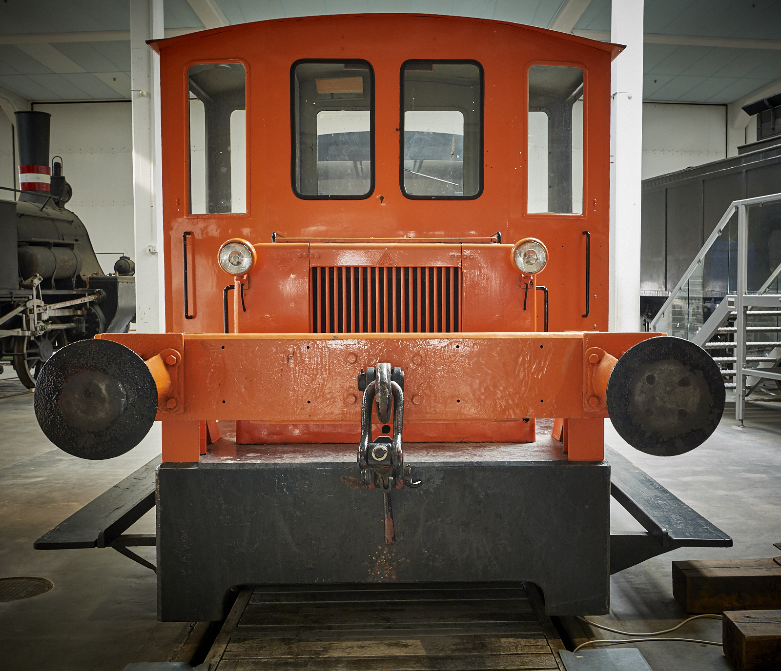 The orange rail-car mover is exhibited among the huge steam engines